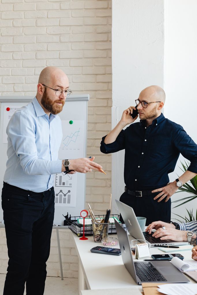 Colleagues in corporate attire discussing work at an office meeting, with one on a phone call.